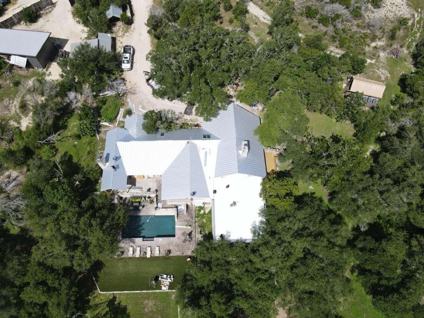 Aerial view of a standing-seam metal roof set among mature oak trees